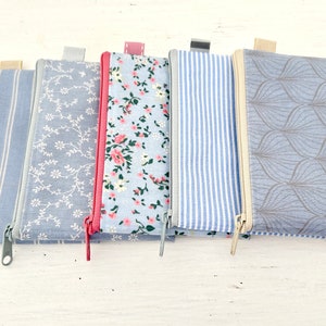 May include: Five zippered pouches with different patterns. The pouches are all made of a light blue fabric with a white pattern. The patterns include stripes, floral, and geometric designs.