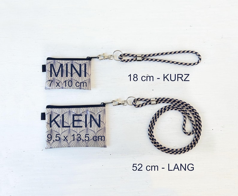 May include: Two beige fabric pouches with black text and geometric patterns. The smaller pouch says "MINI 7 x 10 cm" and the larger pouch says "KLEIN 9.5 x 13.5 cm".  Two black and white patterned cords are included, one is 18 cm long and the other is 52 cm long.