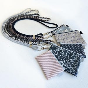 May include: Five small fabric pouches with different patterns, including floral, geometric, and polka dots, attached to a black and gray lanyard.