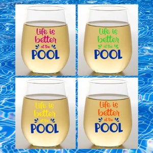 May include: Four stemless wine glasses with the text "Life is better at the POOL" in different colors. The glasses are filled with a clear liquid, possibly wine or water. The background is a blue and white tiled pool.