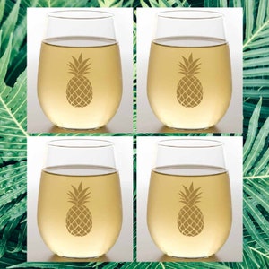 May include: Set of four clear glass wine glasses with a pineapple design etched on the front. The glasses are filled with a light yellow liquid.