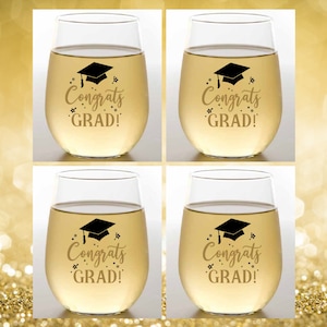 May include: Set of four clear glass wine glasses with gold lettering that reads "Congrats Grad!" and a black graduation cap graphic.