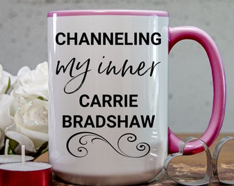 May include: White ceramic mug with a pink rim and handle. The mug has black text that reads "Channeling my inner Carrie Bradshaw".