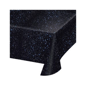 May include: A black tablecloth with a speckled pattern of white and blue dots. The tablecloth is made of a smooth, shiny material and has a folded edge. The overall theme is a celestial or space-themed design.