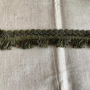 Könnte beinhalten: Grüner Fransenbesatz mit einem dekorativen Wellenmuster. Dieser Besatz ist perfekt, um Vorhängen, Kissen oder anderen Heimtextilien einen Hauch von Eleganz zu verleihen.