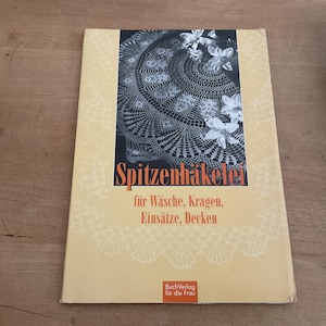 May include: A vintage book titled "Spitzenhäkelei" with a cream-coloured cover. The cover features a black and white crochet design, white flowers, and text in German. The book is for washing, collars, inserts, and blankets.