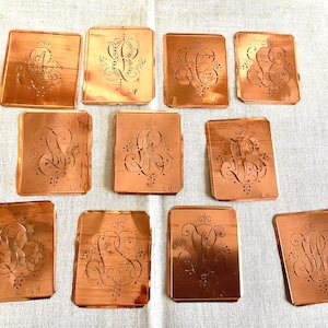 May include: Ten antique copper stencils for embroidery or other crafts. Each stencil features a different ornate design with initials "LJ", "LM", or "LN".