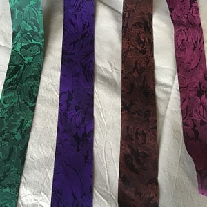 Könnte beinhalten: Vier verschiedene gemusterte Bandborten mit Blumendesigns. Die Bänder sind in den Farben Grün, Lila, Braun und Rosa.
