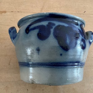 Könnte beinhalten: Ein kleiner, runder Topf aus blau-grauer Keramik mit zwei Henkeln. Der Topf hat einen dunkelblauen Rand und dekorative dunkelblaue Muster. Der Topf steht auf einer hellbraunen Holzoberfläche.