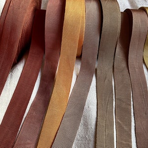 Könnte beinhalten: Acht Spulen mit braunem, beigefarbenem und olivgrünem Grosgrainband. Das Band ist in einer Reihe angeordnet, wobei die Spulen übereinander gestapelt sind.