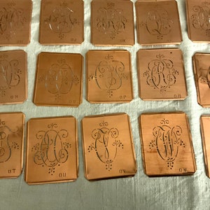 Könnte beinhalten: Ein Satz von 15 antiken Metallschablonen zum Erstellen von Monogrammen. Die Schablonen sind aus Kupfer und haben komplizierte Designs. Jede Schablone ist mit einem Buchstaben des Alphabets beschriftet.