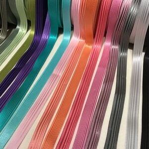 Könnte beinhalten: Sortiment an gestreiftem Satinband in verschiedenen Farben, darunter Schwarz, Grau, Weiß, Rosa, Orange, Türkis, Lila und Grün.