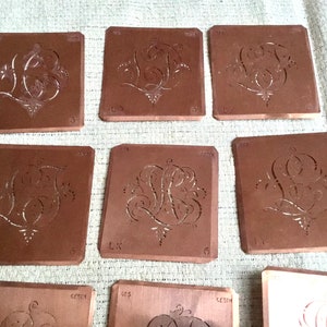 May include: Nine brown rectangular stencils with intricate cut-out designs of cursive letters and floral motifs. The stencils are arranged in three rows of three.