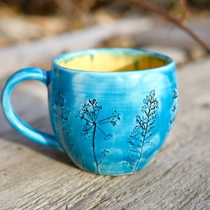 May include: A blue ceramic mug with a yellow interior and a design of stylized plants on the side.
