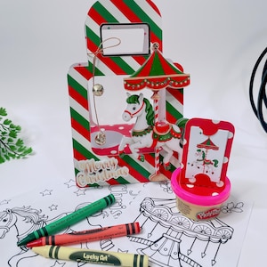Könnte beinhalten: Eine weihnachtliche Geschenktüte mit einer Karussellfigur, einer Halskette, Buntstiften und einem Play-Doh-Behälter. Die Tasche hat rot, grün und weiße Streifen. Buntstifte sind grün, rot und gelb. Der Text auf den Buntstiften lautet: "Je härter du arbeitest, desto mehr Glück hast du."
