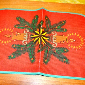 May include: Red Christmas table runner with a green pine tree design and two candles with yellow flames. The design is symmetrical and features a yellow star in the center.
