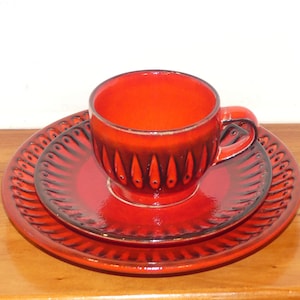 Könnte beinhalten: Ein rotes Keramik-Teetassen- und Untertassen-Set mit einem schwarzen und roten geometrischen Muster. Tasse und Untertasse haben eine glänzende Oberfläche.