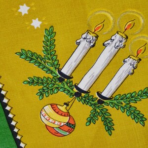 May include: A yellow textile with a festive design. Three white candles with orange flames are surrounded by green sprigs and a colorful ornament. White stars and a green border with black and white accents complete the design.