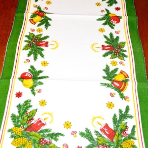 May include: A white table runner with a green border and a Christmas-themed design. The design features red candles, green pine branches, yellow stars, red berries, and gold bells.