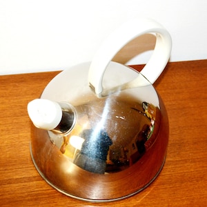 May include: A stainless steel kettle with a white handle and spout cover. The kettle has a rounded body and a shiny, reflective surface. The handle is arched, and the spout cover is cylindrical. The kettle is designed for stovetop use.