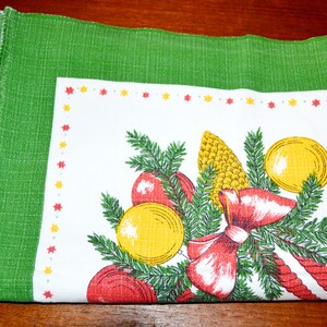May include: A white tablecloth with a green border and a Christmas-themed design. The design features a red bow, pine branches, yellow ornaments, and a red and white candy cane.