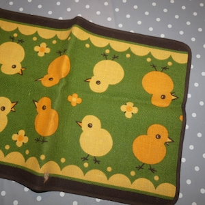 May include: A green and yellow kitchen rug with a pattern of chicks and flowers. The rug has a brown border.