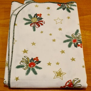 May include: White tablecloth with a festive Christmas design featuring green holly sprigs, red berries, gold stars, and bows. The tablecloth has a black trim around the edges.