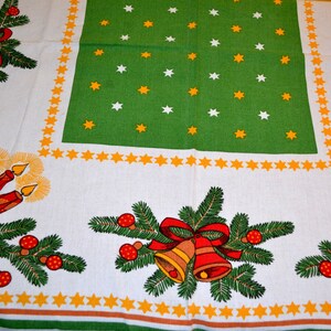 May include: A white tablecloth with a green border and a repeating pattern of yellow stars. The tablecloth features a Christmas theme with images of candles, bells, and pine branches.