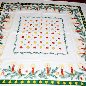 May include: White tablecloth with a green and yellow border featuring a repeating pattern of stars, candles, and pine branches. The tablecloth is perfect for a Christmas dinner.