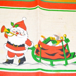 May include: A red and green Christmas placemat with a white background. Santa Claus is depicted in the center of the placemat, blowing a trumpet and pulling a sleigh full of presents.