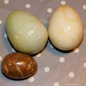 May include: Three decorative eggs made of polished stone. One egg is green, one is white with brown streaks, and one is brown with white streaks.
