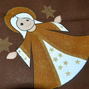 May include: A brown fabric angel with a white dress and gold stars. The angel has a halo and a smiling face.