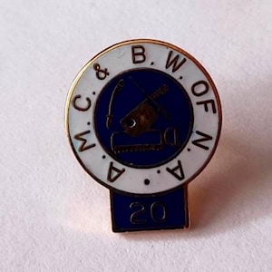 Pode incluir: Alfinete de lapela dourado com um emblema azul e branco. O emblema apresenta texto e um gráfico de ferramentas. O alfinete tem um verso dourado e uma base retangular azul com o número 20.