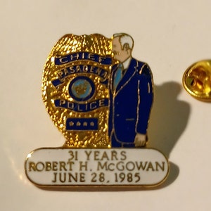 Puede incluir: Pin de insignia de policía dorada y azul con el retrato de un hombre con un traje azul. La insignia dice "Chief Pasadena Police" y el texto debajo dice "31 Years Robert H. McGowan June 28, 1985".