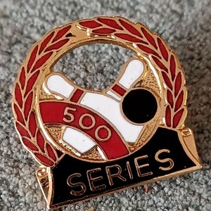 May include: Gold-colored bowling pin pinback button with a red and white bowling pin design and a black banner with the text "500 SERIES".