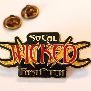 May include: A gold and black enamel pin with the text "SoCal Wicked Fastpitch" in gold lettering. The word "Wicked" is in red lettering.
