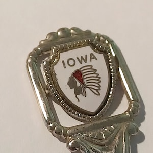May include: Silver souvenir spoon with a white enamel design featuring an American Indian headdress and the word "IOWA".