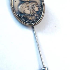 May include: A bronze pin featuring a depiction of three people and the text "Centennial United Methodist Women".