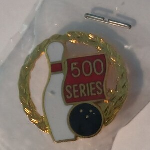 May include: Gold-colored bowling pin and ball pin with a red and white banner that says "500 SERIES" in a gold wreath.