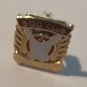 May include: Gold-colored bowling pin 500 Club pin with a red and white banner.