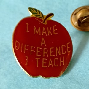 May include: Red apple-shaped pin with gold trim and the text "I make a difference I teach".