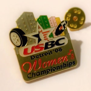 May include: Gold pin featuring a red, white and blue star, a black car and a cityscape. The text reads "USBC Detroit '08 Women's Championships".