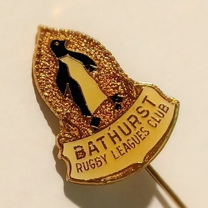 May include: Gold-colored pin with a black and white penguin illustration and the text "Bathurst Rugby Leagues Club".