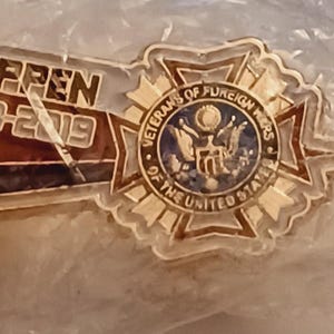 May include: Gold-colored pin with a blue and white emblem that reads "Veterans of Foreign Wars of the United States".
