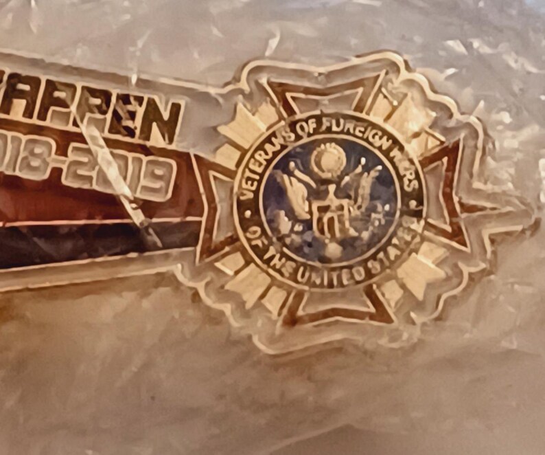 May include: Gold-colored pin with a blue and white emblem that reads "Veterans of Foreign Wars of the United States".