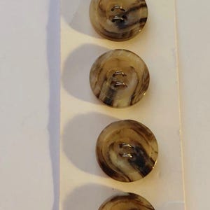 May include: Four round buttons with a marbled brown and tan pattern are displayed on a white card. The card has the text "Casa de Leon" at the top and "U. S. A." at the bottom. Each button has two holes for sewing.