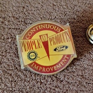 May include: A gold and red pin with the text "Continuous People and Products Improvement" and the Ford logo.