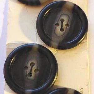 May include: Four dark brown buttons with a marbled effect, attached to a vintage card labeled "Le Chic." Each button is approximately 1 1/8 inches in diameter and has four holes. The card reads "Guaranteed Washable."