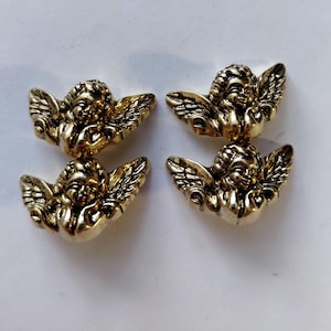 May include: Four gold-colored cherub figurines with detailed wings and smiling faces. The cherubs are arranged in two pairs, each facing the other. The figurines have a metallic finish and are likely decorative elements.