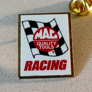 May include: A white and gold pin with a checkered flag and a red circle with the words "MAC QUALITY TOOLS" and the word "RACING" in red letters.